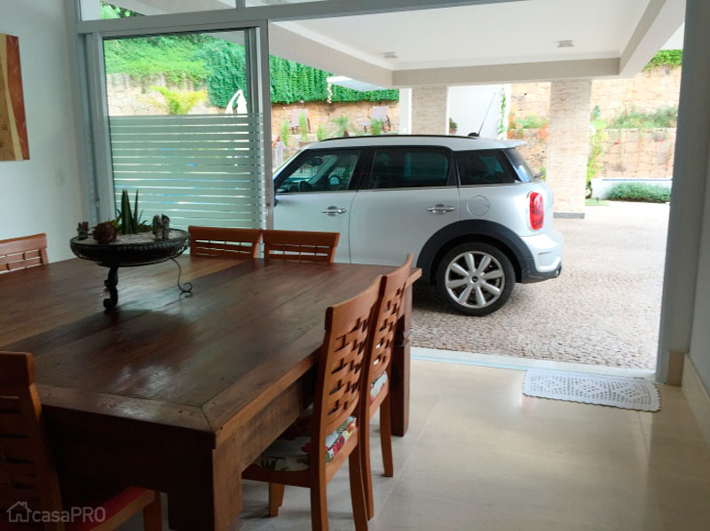 O espaço da garagem fica integrado ao espaço gourmet. O material utilizado no piso é o mosaico português. Os pilares são revestidos com tijolos serrados. O vidro da porta possui uma película que esconde os carros quando a porta estiver fechada. Projeto de Rosângela Rodrigues Kazitoris.