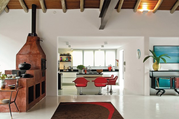 Neste projeto de Neza Cesar, o branco &eacute; quase total, na alvenaria e no piso de cimento polim&eacute;rico. Pinceladas mais fortes aparecem nas cadeiras vermelhas da bancada, no multicolorido dos objetos culin&aacute;rios, no tapete de desenho abstrato e at&eacute; no terracota do fog&atilde;o a lenha, que convive em harmonia com o ambiente contempor&acirc;neo.
