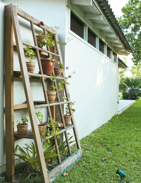 Com uma porta de correr velha e restos de madeira, Jorge montou um jardim vertical na lateral da construção. À noite, um holofote destaca o arranjo.