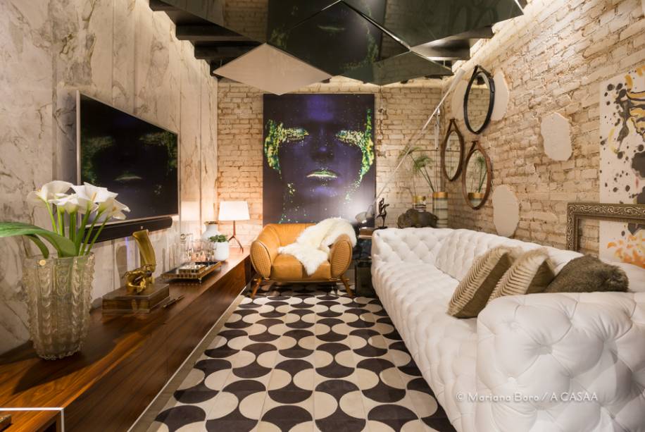 Os tons terrosos e laranjas dos tijolos maciços e a presença dos veios de madeira no teto do porão, que constam da construção original, ditaram a paleta de cores escolhida por Alexandre Müller e Marcelo Wolschick. A metragem reduzida, de 12,37m², conduziu a proposta de uma sala intimista para um casal relaxar. O painel da TV foi valorizado pelo Mármore Paraná Nuvolato, enquanto as demais paredes trazem uma pegada mais destroyed. O teto vem com uma instalação de painéis irregulares iluminados com fitas de LED. Os tons terrosos e laranjas dos tijolos maciços e a presença dos veios de madeira no teto do porão, que constam da construção original, ditaram a paleta de cores escolhida por Alexandre Müller e Marcelo Wolschick. A metragem reduzida, de 12,37m², conduziu a proposta de uma sala intimista para um casal relaxar. O painel da TV foi valorizado pelo Mármore Paraná Nuvolato, enquanto as demais paredes trazem uma pegada mais destroyed. O teto vem com uma instalação de painéis irregulares iluminados com fitas de LED.