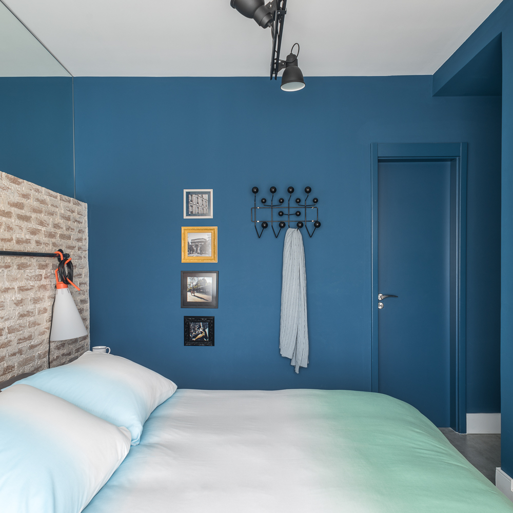 Quarto com parede azul; cabideiro; cabeceira de tijolinhos; roupa de cama tie dye