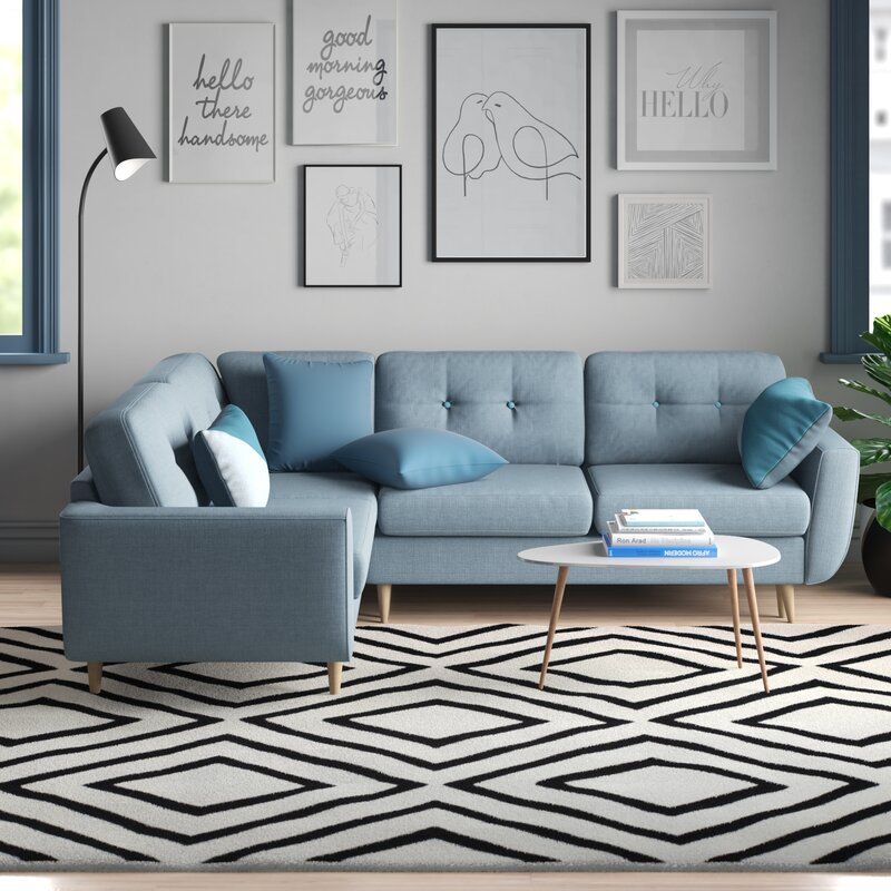 Sofá em L azul; tapete geométrico preto e branco; quadros na parede