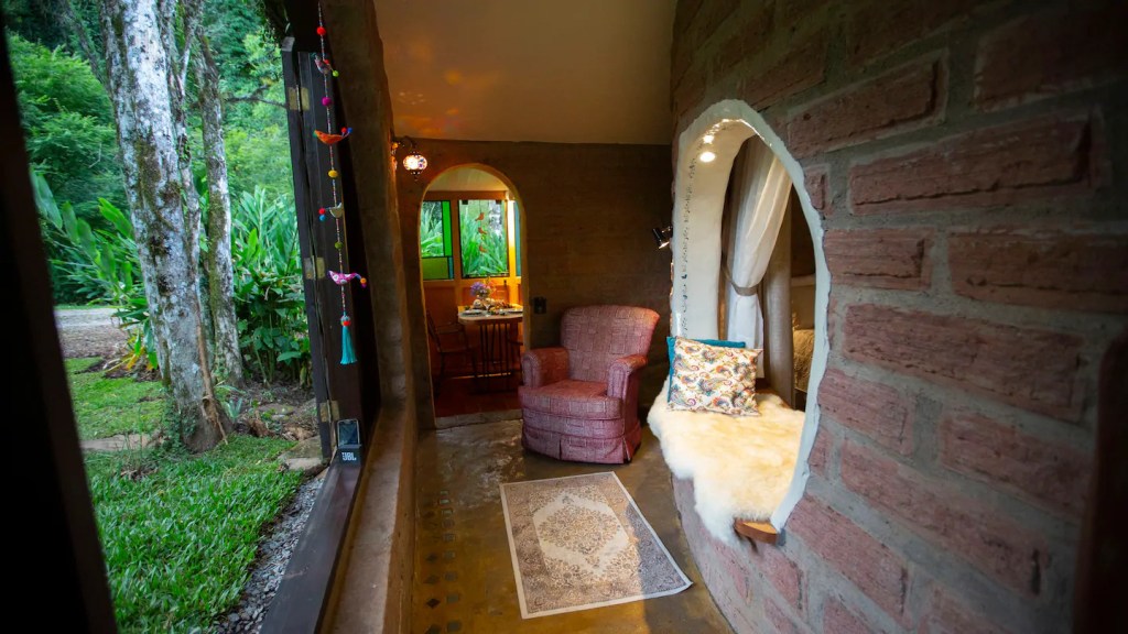 Hall de entrada de tijolos laranjas, com uma poltrona vermelha, um tapete estampado e um peitorial da janela arredondado com almofadas para sentar.