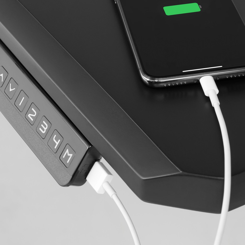 Lateral da mesa com a entrada USB com um fio branco conectado à ela e a um celular que está carregando
