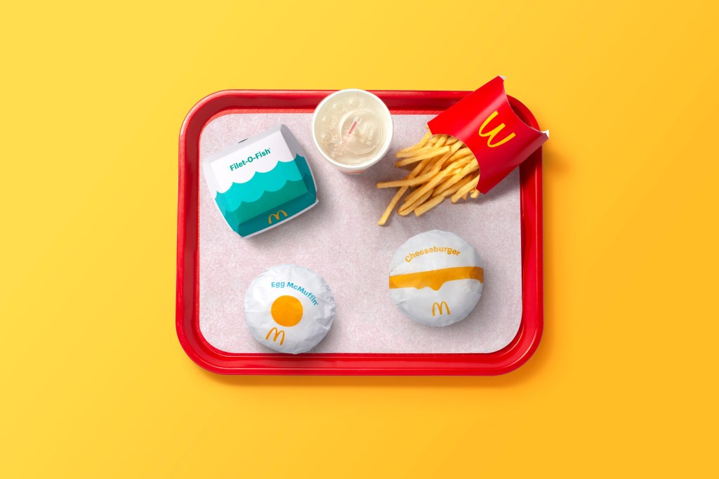Bandeja vista de cima com cheeseegg, cheeseburguer, batata frita e caixa de mcfish com ondas azuis. Copo de refrigerante visto de cima