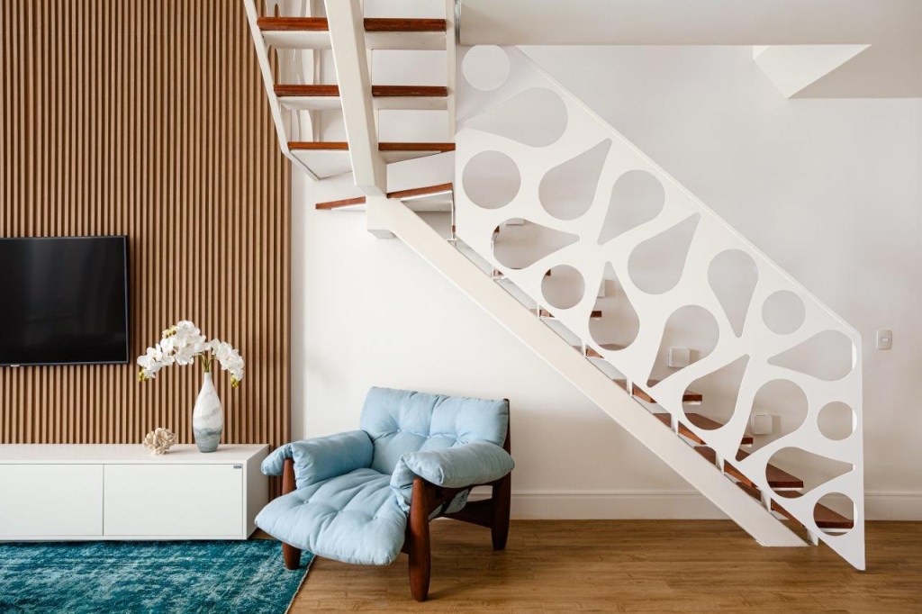 Escada branca com guarda-corpo metálico e furos em formato de gota. Poltrona Mole de Sergio Rodrigues.