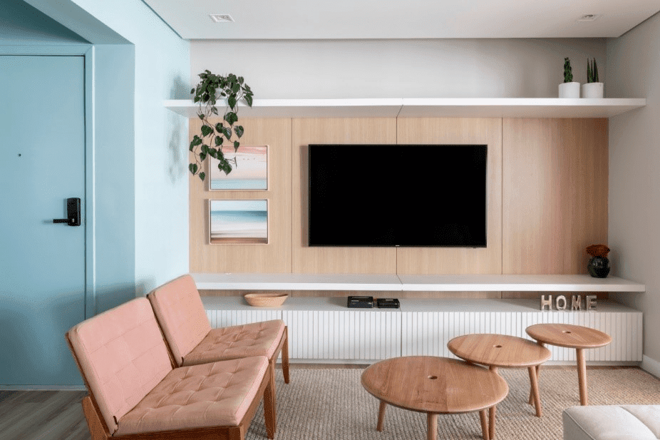 Sala de estar com Tv no painel de madeira clara, à esquerda a porta colorida turquesa