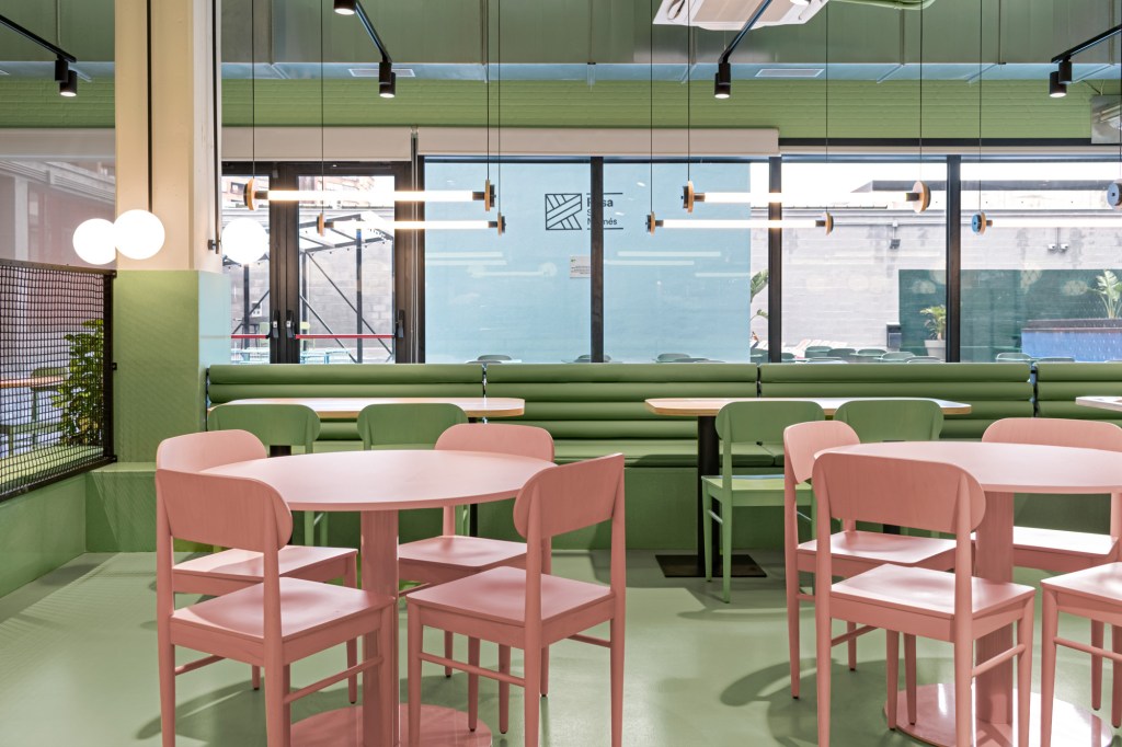 Sala com mesas e paredes verdes, com os acentos da parede da mesma cor, e mesas e cadeiras rosas