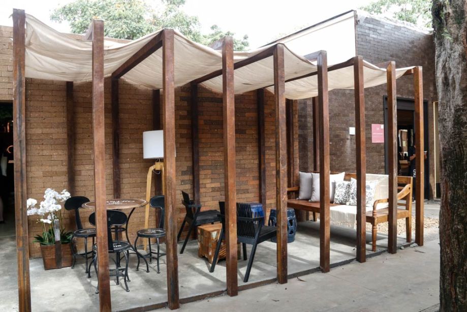 Pergolado de madeira no ambiente externo de um restaurante, com mesas e cadeiras pretas.