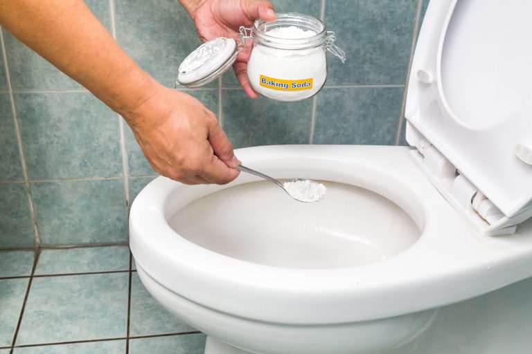 Mão colocando biacrbonato de sódio em vaso sanitário branco