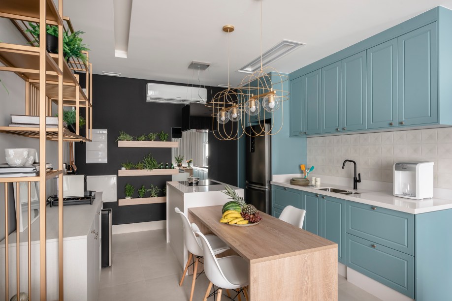 Neste loft com 40m², os armários superiores da cozinha foram projetados na cor azul petróleo e estão localizados acima da pia da geladeira, possibilitando uma melhor organização dos utensílios no projeto de interiores realizado pelas profissionais do escritório Meet Arquitetura