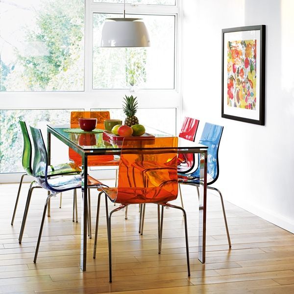 Sala de jantar com seis lugares. Cadeiras laranjas, azuis, vermelhas e verdes. Grande janela ao fundo