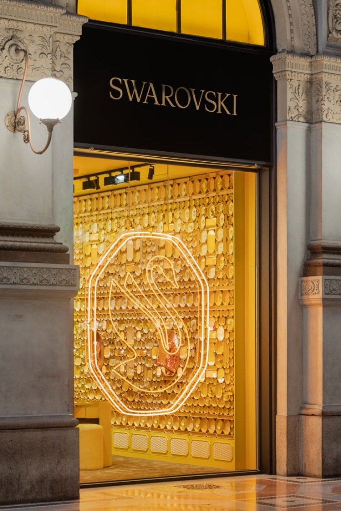 Foto vertical da fachada da loja com logo de cisne iluminado no vidro.