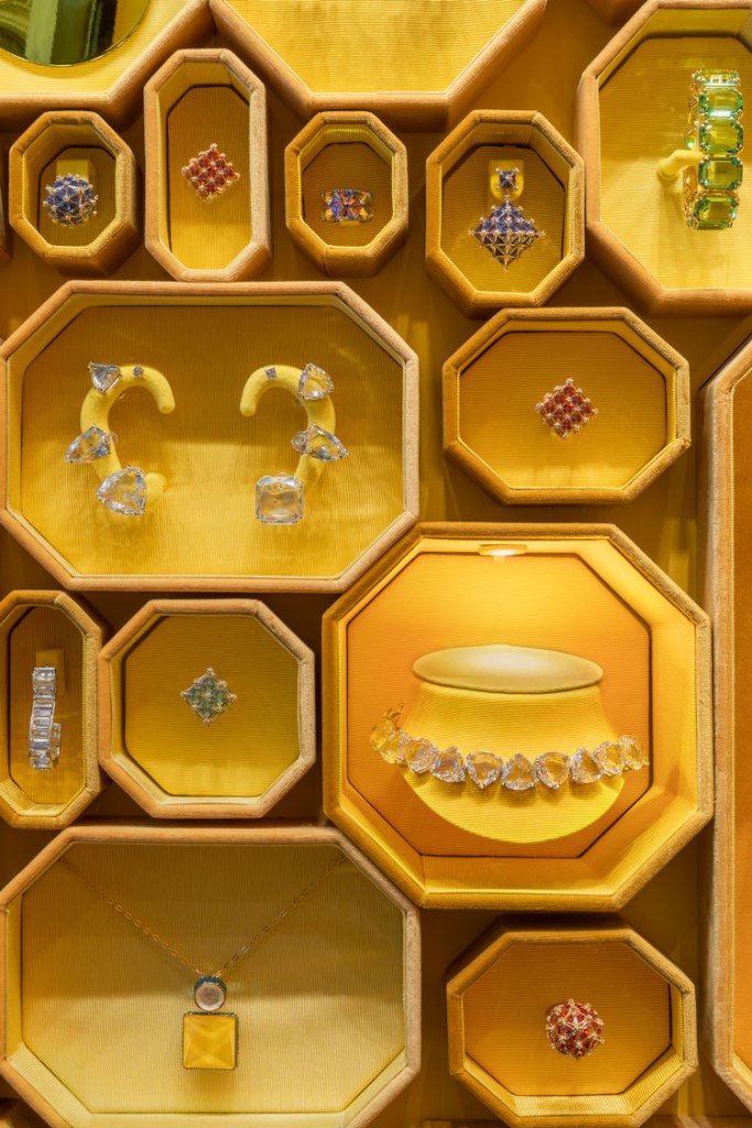 Detalhe das joias, brincos, colares e aneis nas caixas octogonais amarelas na parede 