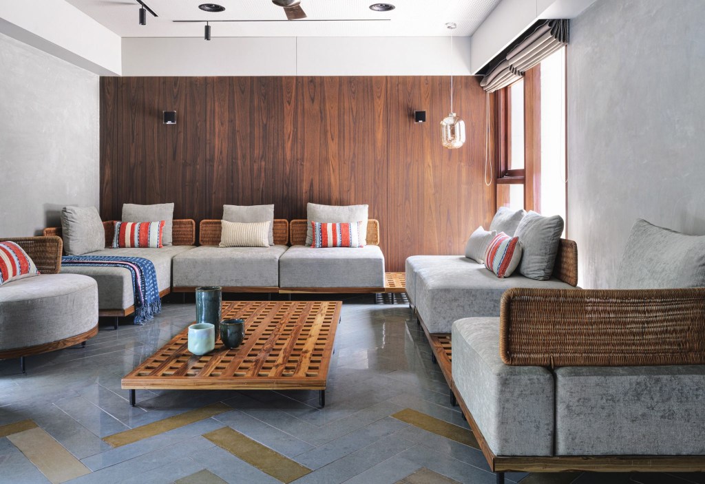 Sala de estar minimalista com sofá cinza, com almofadas coloridas e madeira em uma das paredes