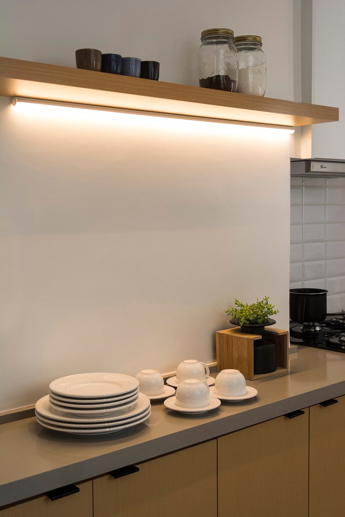Cozinha com led integrado na estante acima do buffet com tampo cinza e portas de madeira clara