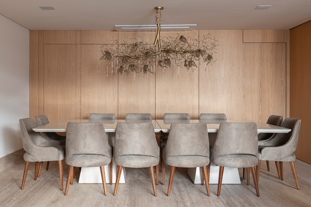 Sala de jantar com mesa de doze lugares, com pendente acima da mesa. Forro de drywall, piso de madeira, assim como os armários na parede do cômodo