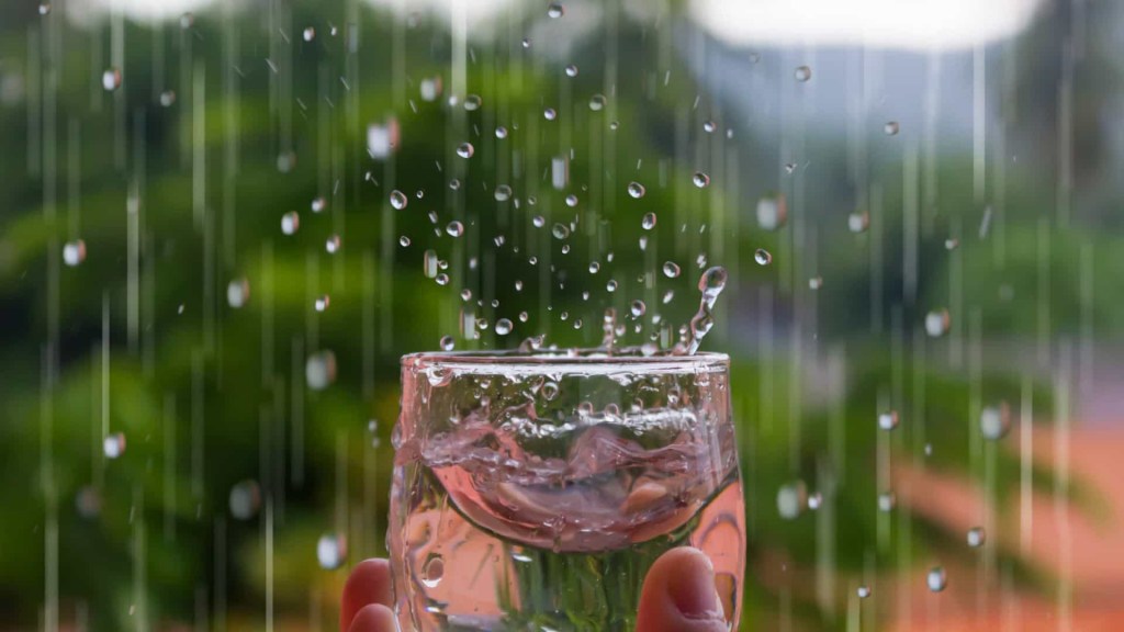 Mão segurando copo transparente em vidro armazenando água da chuva