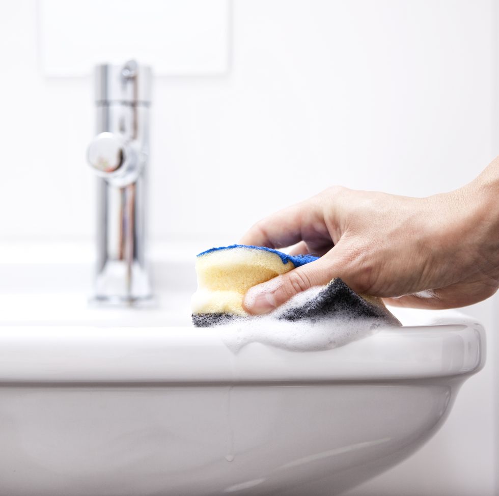 Mão limpando pia branca com esponja amarela
