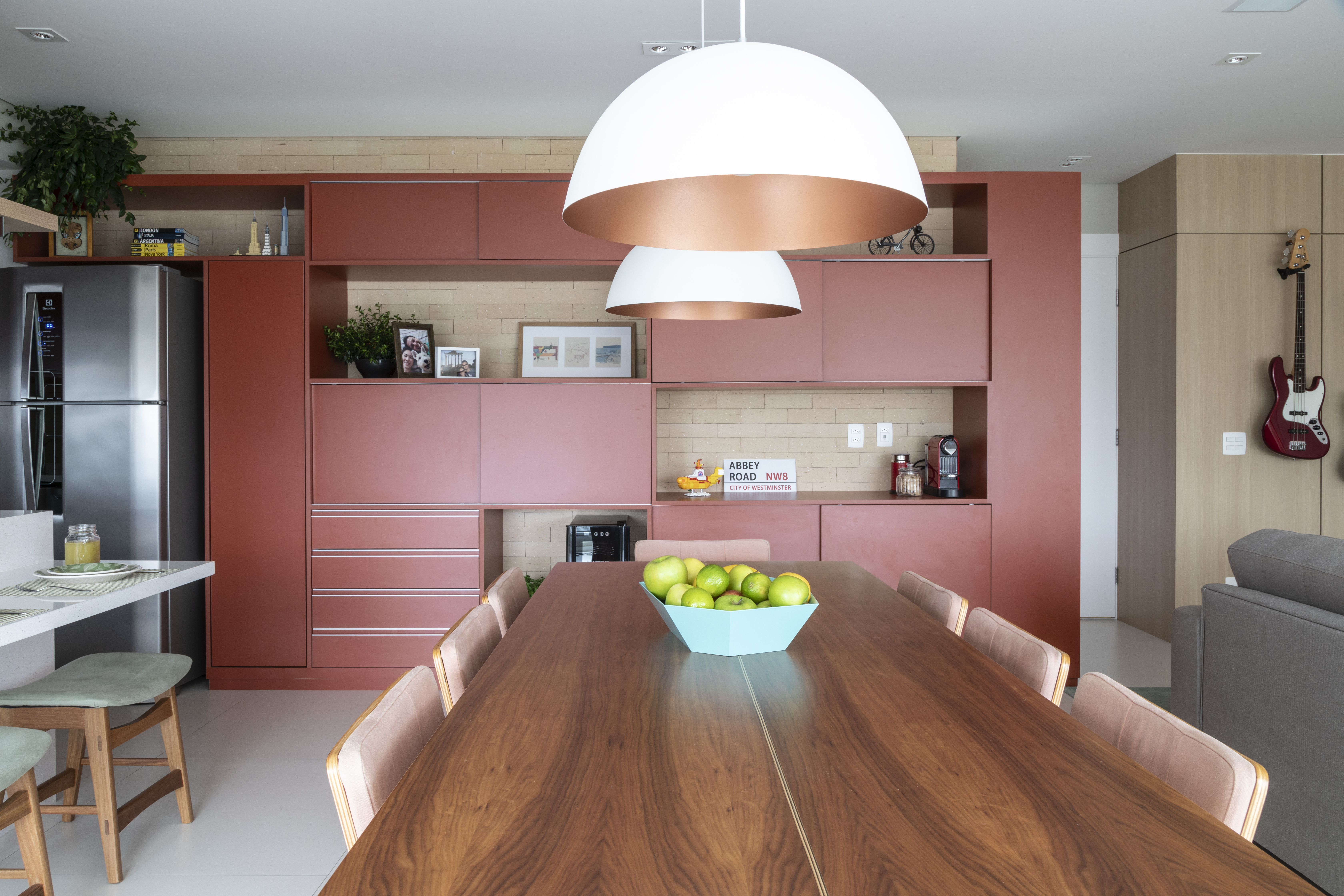 Arm&aacute;rios na cor goiaba na parede do fundo, com uma mesa de jantar de madeira extensa em primeiro plano.