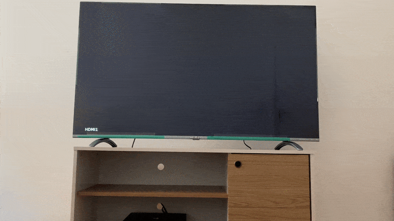 Gif com um controle aparecendo de baixo, mão aperta um dos botões e na TV Britânia 55