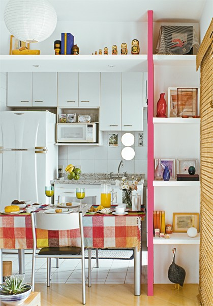O v&atilde;o entre a sala e a cozinha veio abaixo e foi emoldurado com prateleiras de gesso no alto e em uma das laterais - nesta, est&atilde;o apoiados em um painel pintado de rosa-fosco. Dois espelhos redondos foram colados nos azulejos sobre a pia.