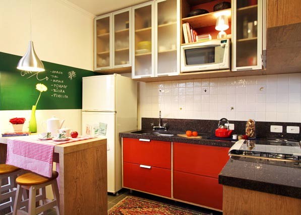 A cozinha projetada pela arquiteta Thais Lenzi Bressiani utiliza o vermelho no arm&aacute;rio e em diversos acess&oacute;rios . Na parede, uma tinta que imita lousa &eacute; utilizada para anotar recados e receitas. Para n&atilde;o pesar no ambiente, os arm&aacute;rios ganharam portas transl&uacute;cidas.