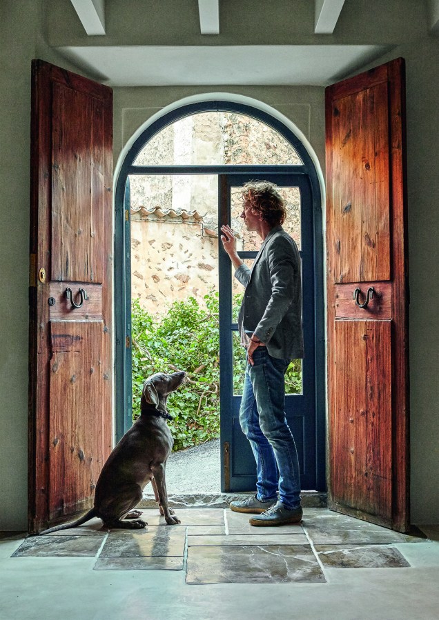 O designer Oro del Negro e sua cachorra, Pearl, em frente à porta de entrada (feita de carvalho por Pedro Casanovas, um artesão local). Aldravas forjadas a mão arrematam a peça.