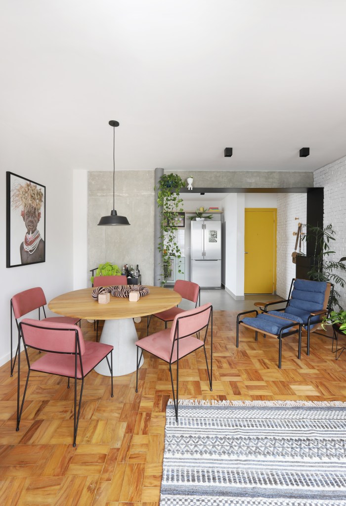 Sala de jantar com mesa com tampo de madeira, cadeiras com estofado rosa.