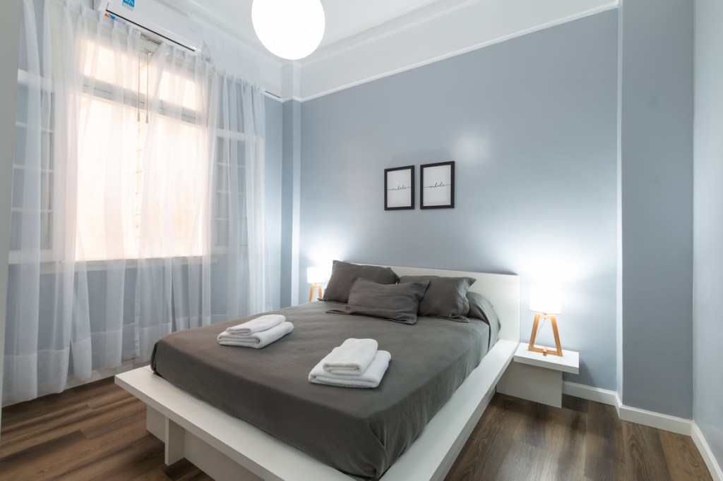 Quarto de casal azul, com roupa de cama cinza e toalhas brancas dobradas em cima da cama