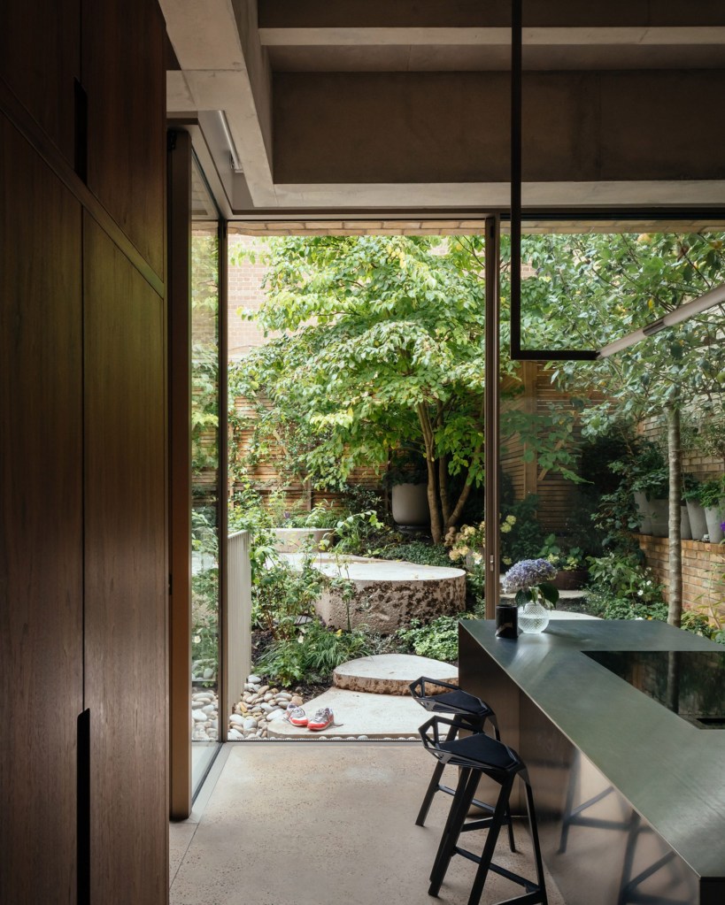 Balcão de café da manhã com duas banquetas de design, com grande armário de madeira e jardim ao fundo, integrado.