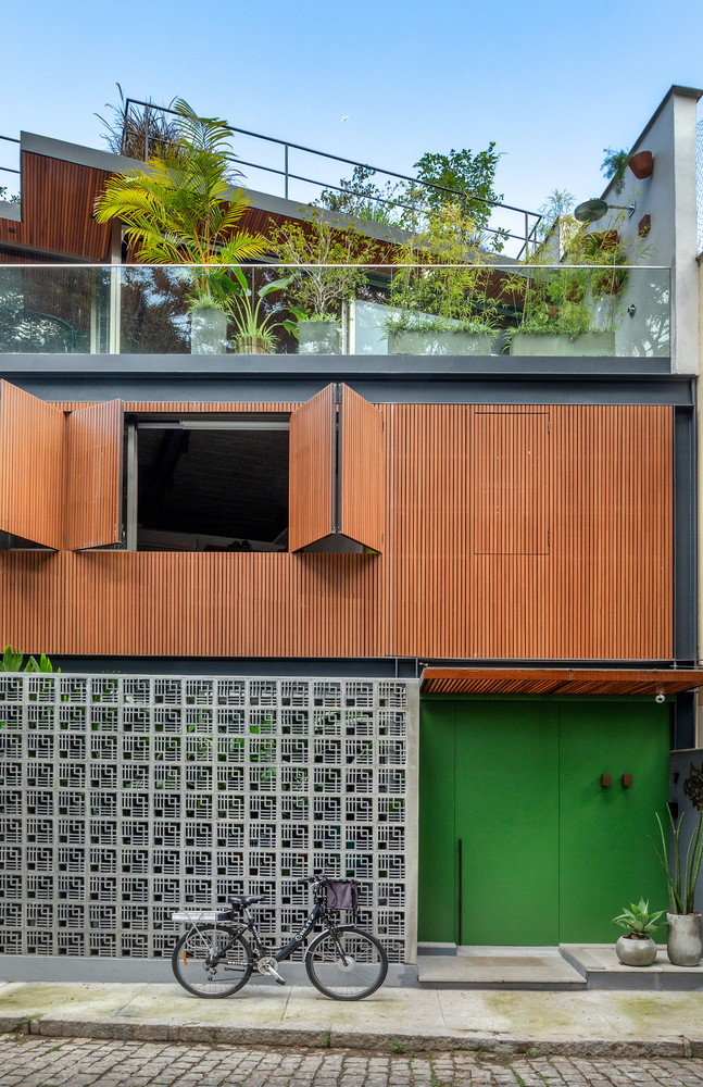Fachada de casa apresenta parede de cobogó e painel de madeira com um solarium e jardim na cobertura