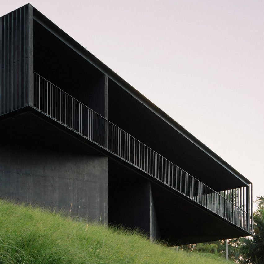 Casa com fachada toda preta com ripado de madeira, grama verde e céu cinza.