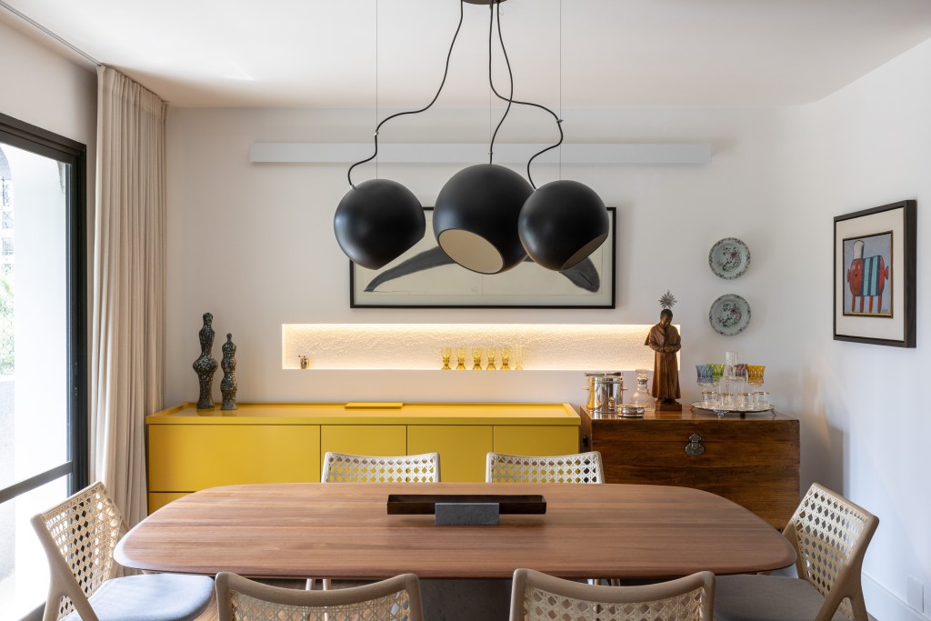 Sala de jantar com pendente; mesa em madeira com quatro lugares; aparador amarelo; nicho iluminado