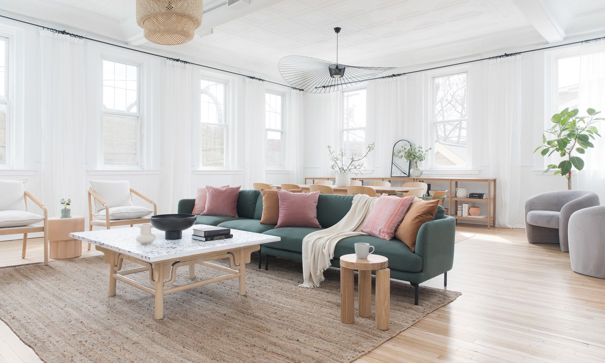 Sala com estilo clean e escandinavo; Sofá verde com almofadas rosa; mesa de centro em madeira; paredes brancas com muitas janelas
