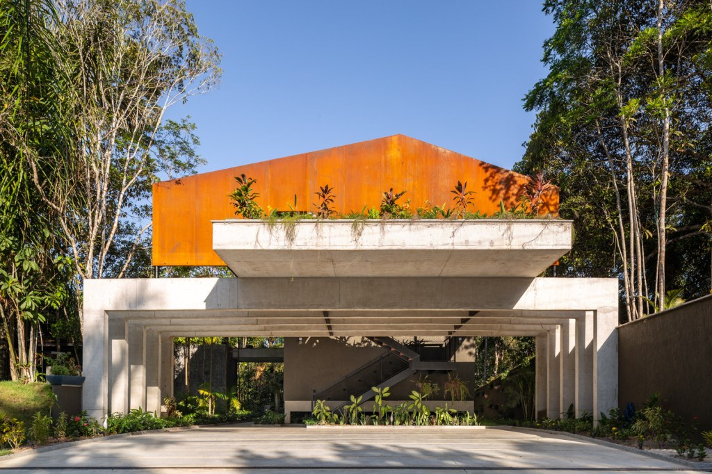 Foto mostra cobertura em aço corten e duas águas, com platibanda sobre estrutura de concreto.