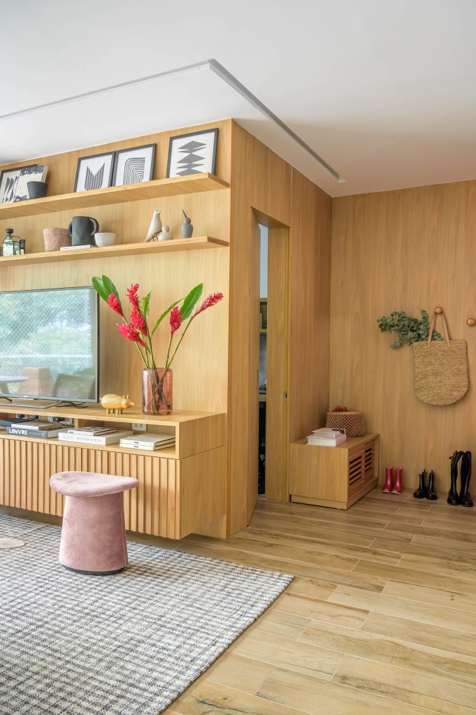 Painel de madeira na entrada de apartamento que vira suporte de TV