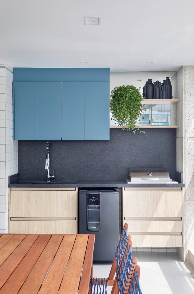 Sala de almoço com armário azul, parede preta e gavetas em madeira com tom claro