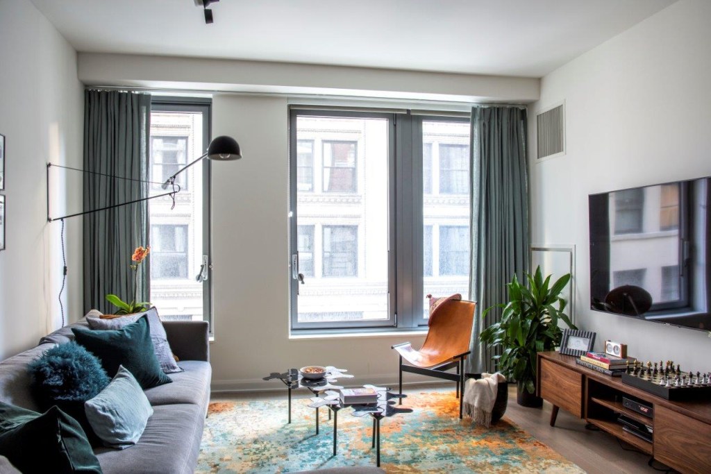 Sala com tapete colorido e mesa de centro; sofá cinza em L