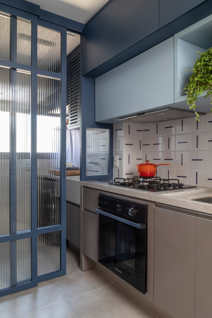 Cozinha com marcenaria azul e backsplash; fogão, lavanderia integrada; porta de vidro