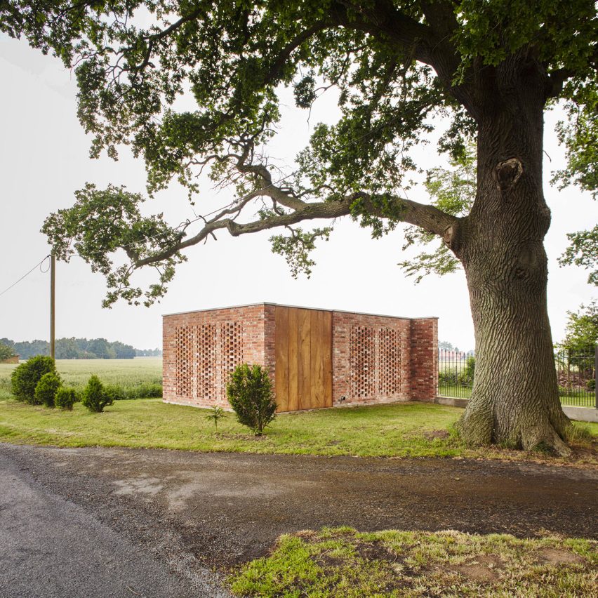 Construção de tijolos vazados com grandes portas de madeiras do piso ao teto em uma área verde.