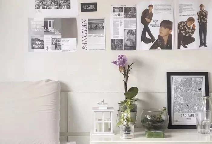 Parede de cabeceira decorada por posteres sem moldura. Sobre a mesinha de cabeceira, um vaso com flor e um quadro emoldurado são os destaques do décor.