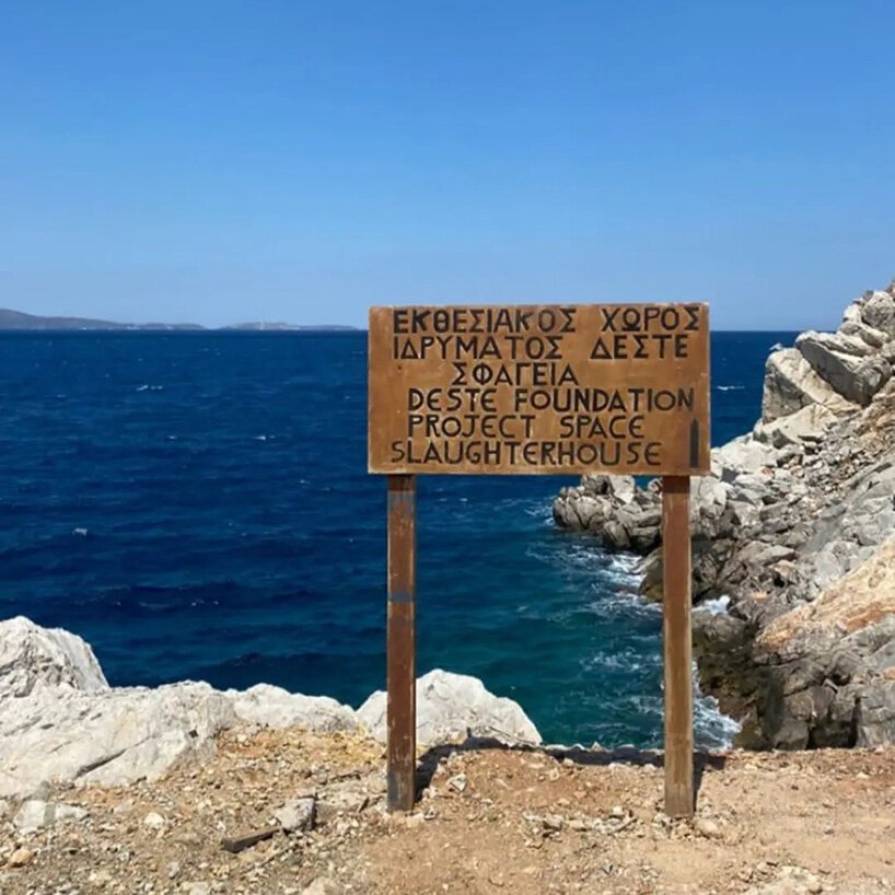 Placa de madeira com escritos em grego diante do mar.
