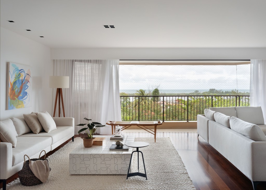 Sala de estar em tons neutros com sofás e tapete, varanda ao fundo