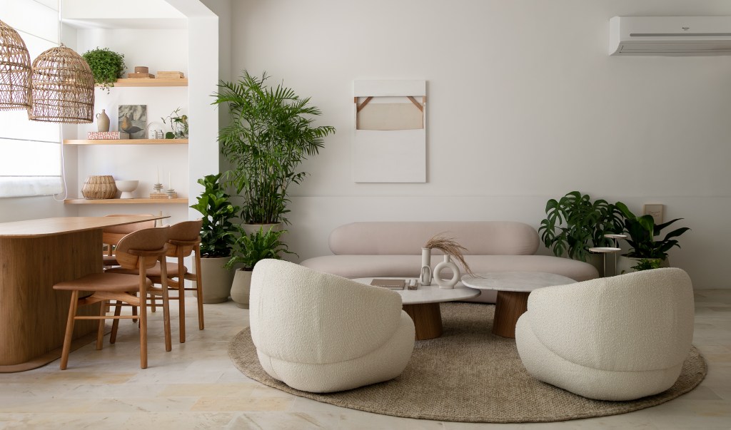 Sala de estar com sofá branco curvo, duas poltronas brancas e mesa de centro em forma curva.