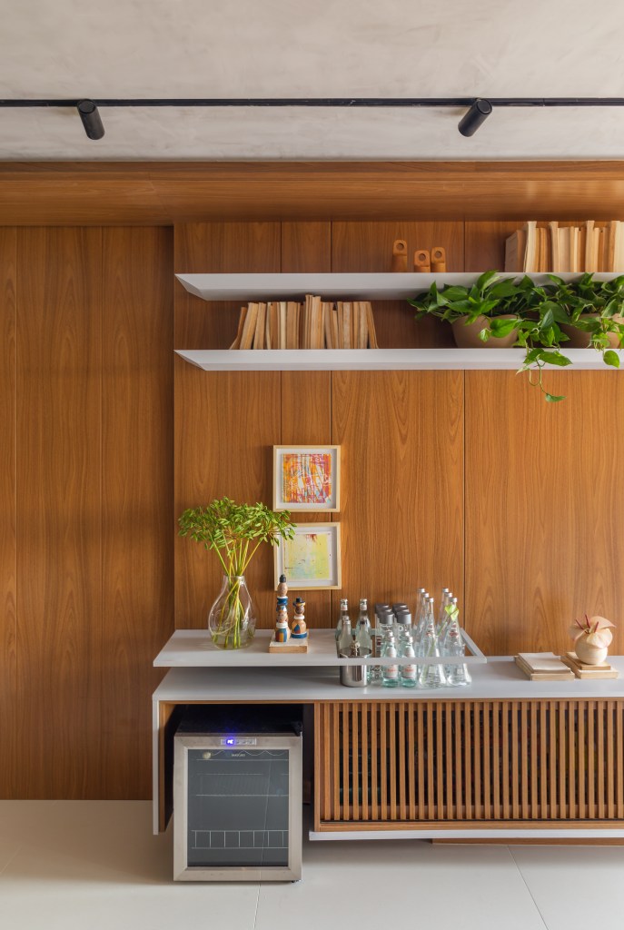 Sala de estar com parede revestida de madeira; rack com cantinho de bar.