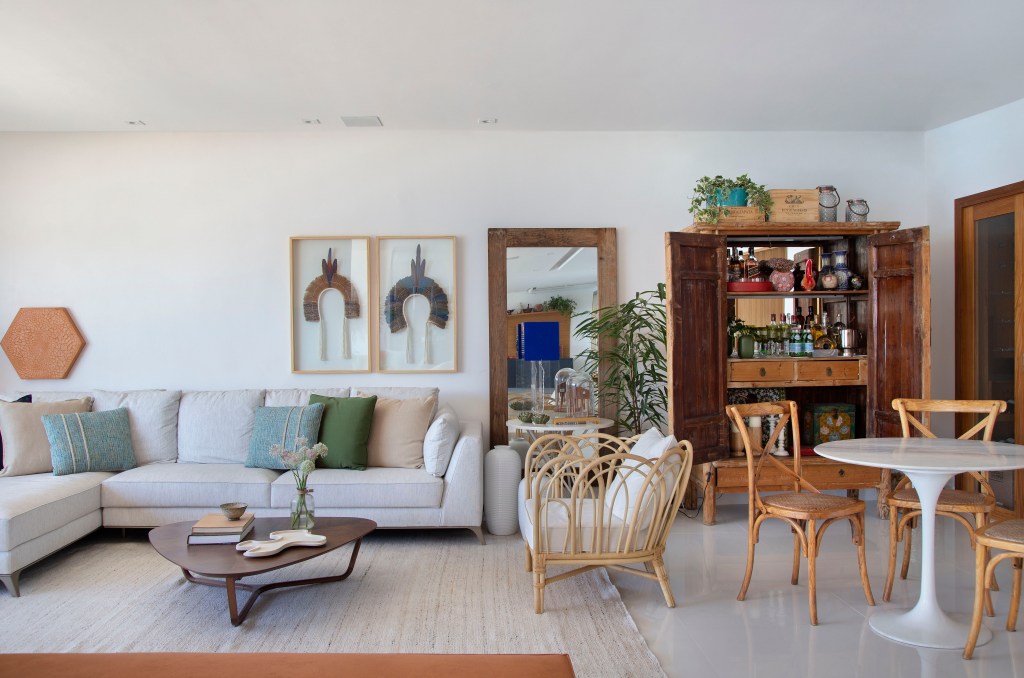 Sala de estar com piso de porcelanato laqueado, grandes janelas e sofá e poltronas claros.