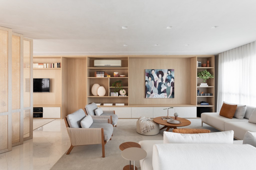 Sala de estar com piso de mármore, sofá branco, poltronas, estante de madeira com nichos e quadro.