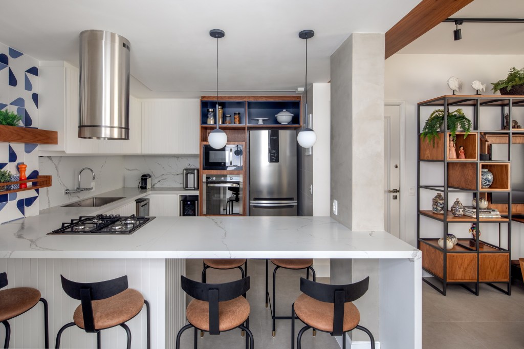Cozinha integrada com marcenaria branca, bancada branca e parede de azulejos azuis.