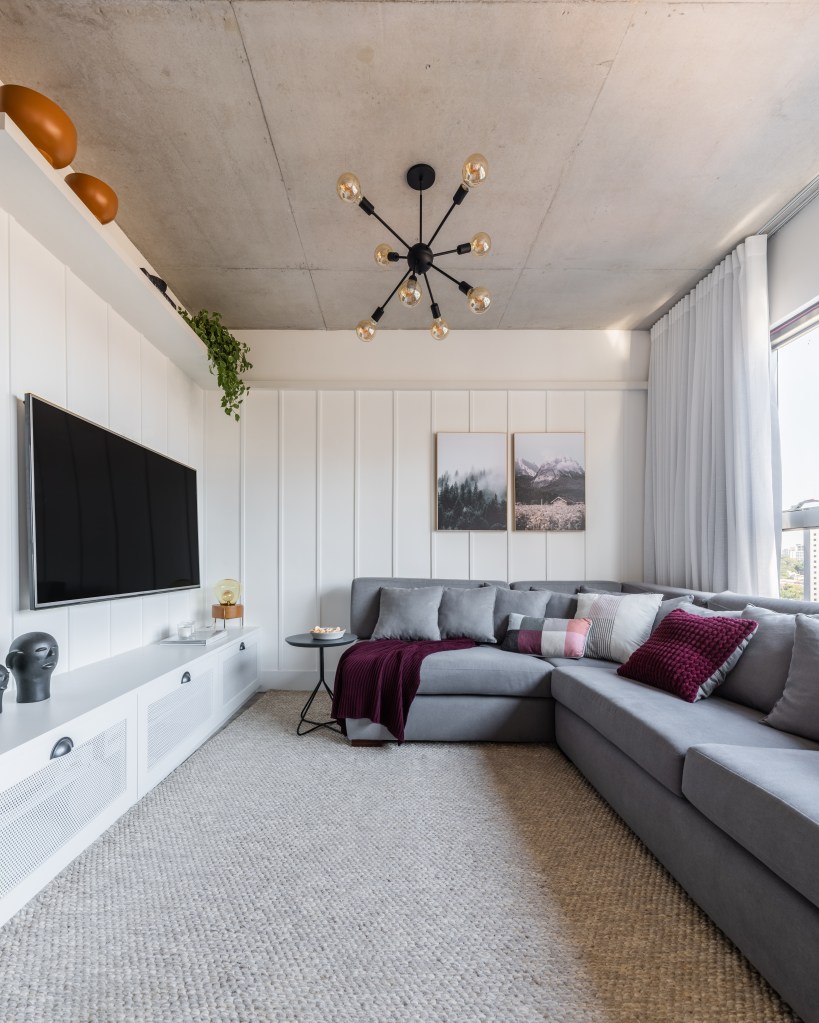 Sala de estar pequena com sofá cinza e parede branca com lambris.